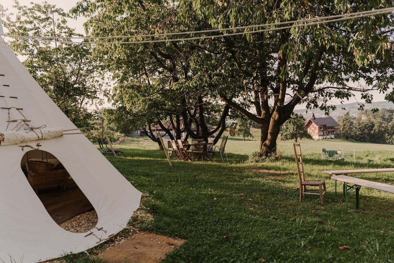 Tipi-Zelt unter Bäumen mit Stühlen und Blick ins Grüne